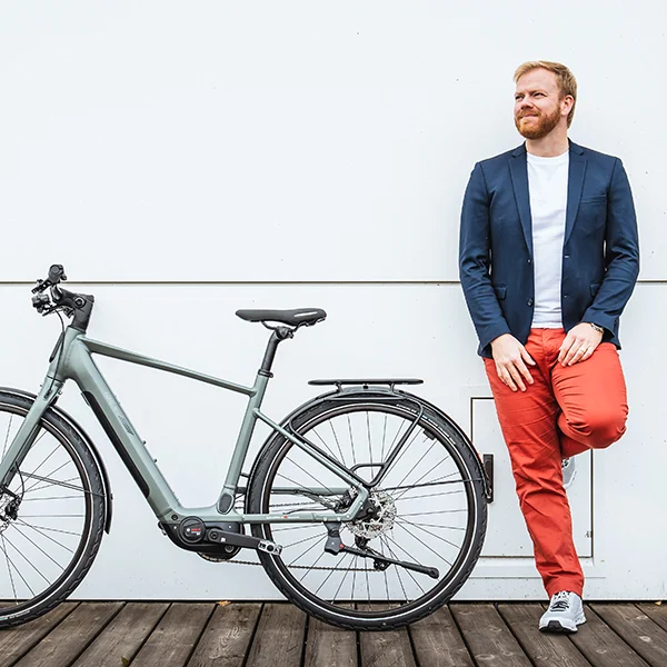 Mann mit roter Hose und blauem Sakko lehnt an einer Wand neben dem Cresta eStrada.